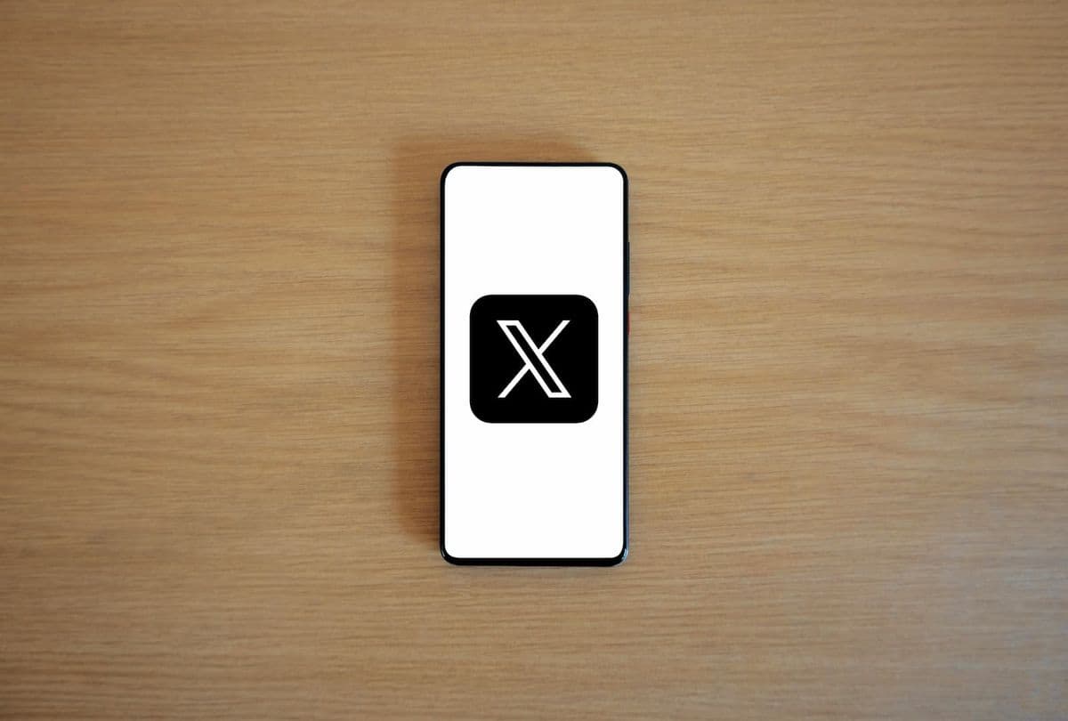 A phone lies on a wooden table, displaying the X logo