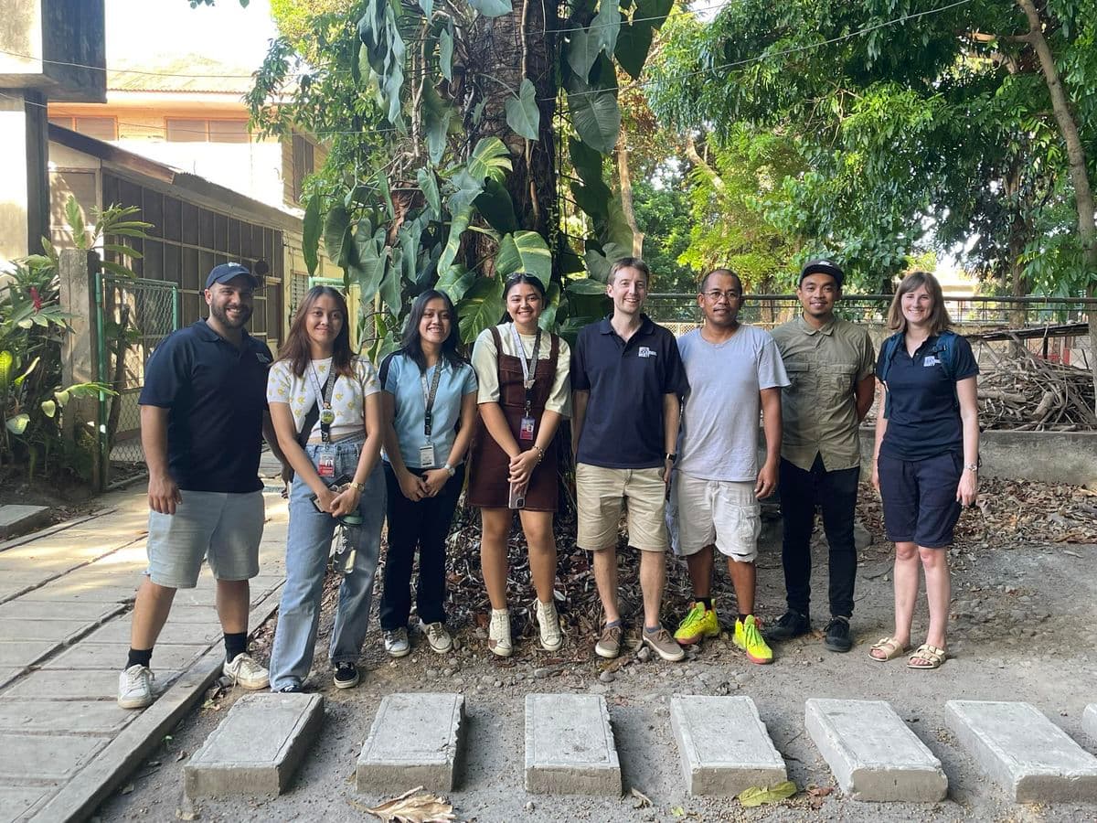 Eight people standing together in front of a tree in the front of a University building in the P